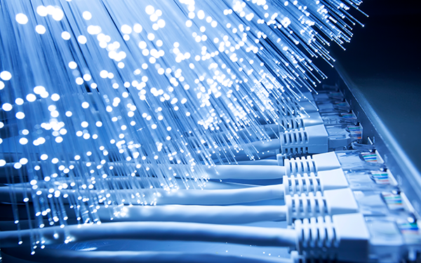 Close-up of glowing fiber optic cables next to several plugged-in Ethernet cables and network ports, representing high-speed internet and data connectivity.